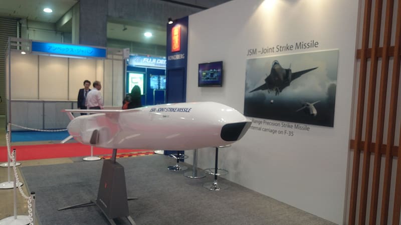 A white full-scale Joint Strike Missile model on a stand at a trade show booth, with an F-35 poster behind it.