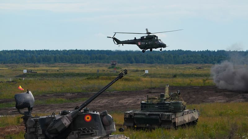 A Polish K2 tank seen from the rear in a field, a Romanian Gepard in the foreground and a W-3 helicopter overhead