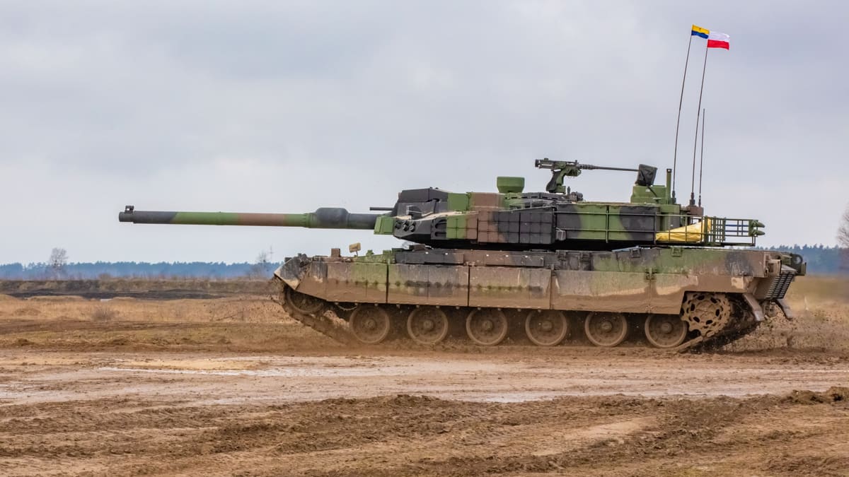 A Polish Army K2 Black Panther tank in green and brown camouflage drives across a muddy firing range under grey sky