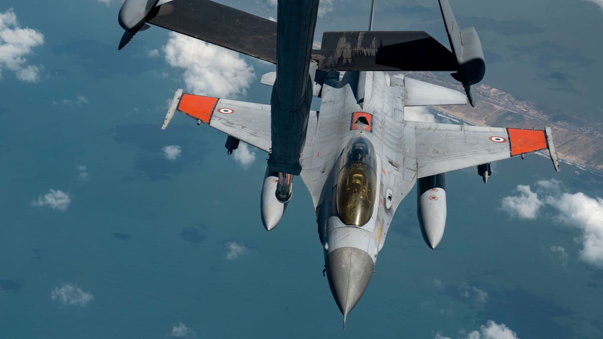 Egyptian F-16 with orange wing panels flying just below a tanker's refuelling boom, high above the sea and coast