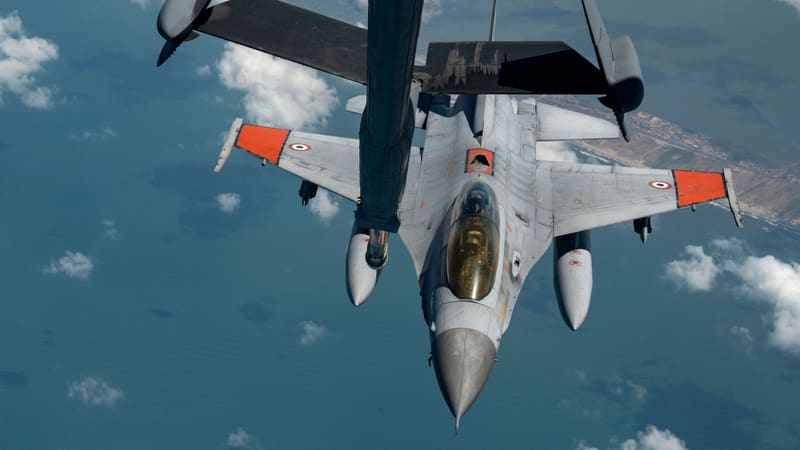Egyptian F-16 with orange wing panels flying just below a tanker's refuelling boom, high above the sea and coast