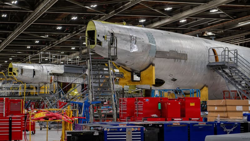 Two stripped, bare-metal KC-135 tanker fuselages on maintenance stands inside a large depot hangar.