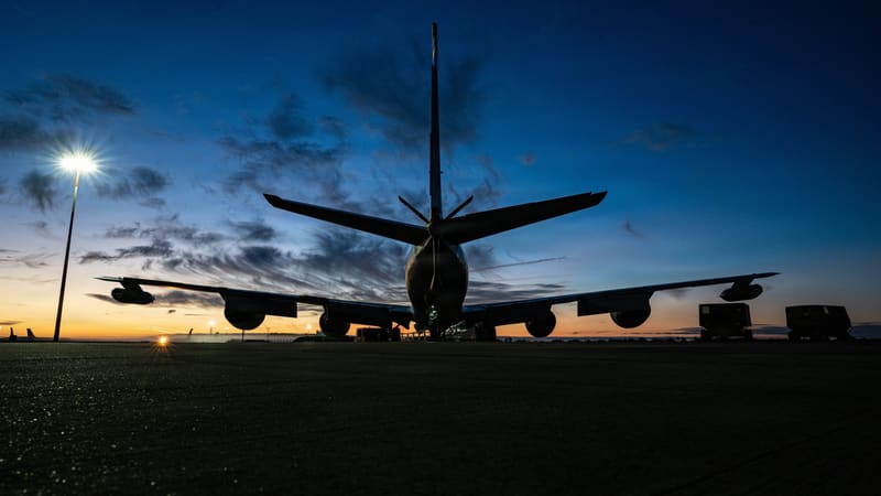 A KC-135 tanker seen from behind on an airfield ramp under a deep blue dusk sky.