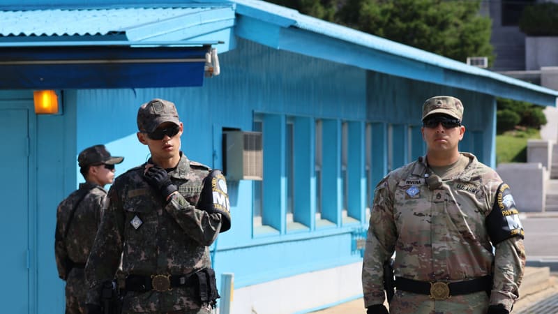 South Korean and U.S. soldiers in sunglasses and UN armbands stand guard beside blue huts at Panmunjom