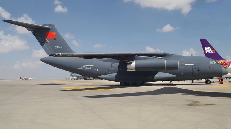 A grey Chinese Air Force Y-20 four-engine transport jet parked on an airshow apron under a cloudy blue sky
