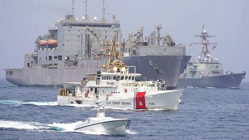 A small white sea drone leads a U.S. Coast Guard cutter, a supply ship and a destroyer across open water