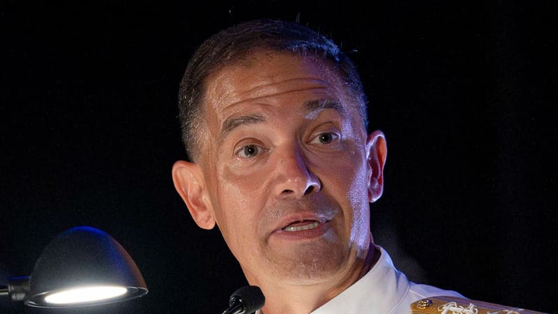 Admiral Brad Cooper in a white dress uniform speaks at a lectern microphone