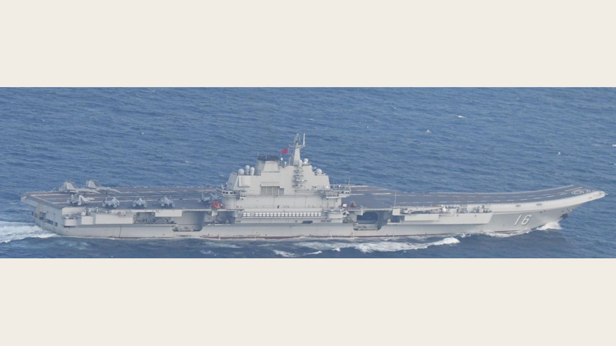 Chinese aircraft carrier Liaoning, hull number 16, sailing in side profile with fighter jets parked on its flight deck