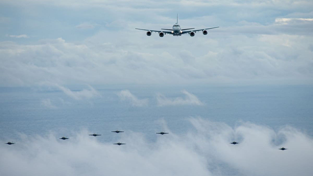 A four-engine Japanese P-1 patrol aircraft flying above clouds with a line of F-35 fighters below it