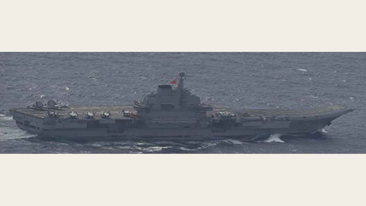 The Liaoning aircraft carrier in grey light with a row of fighter jets parked on its deck behind the island