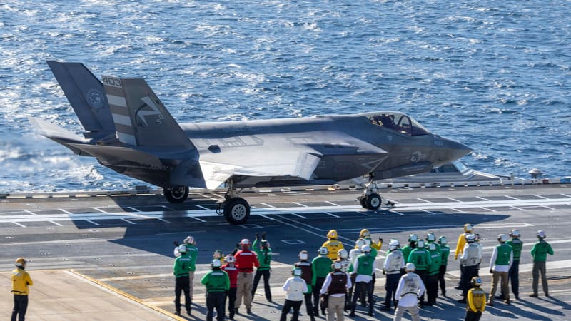 An F-35C fighter on a carrier catapult as flight deck crew in coloured jerseys watch the launch