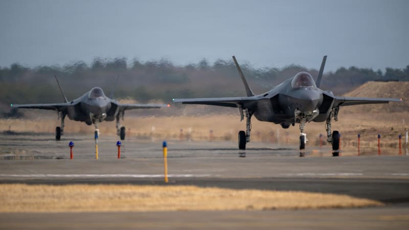 Two Japanese F-35A stealth fighters taxi head-on along a taxiway lined with marker lights