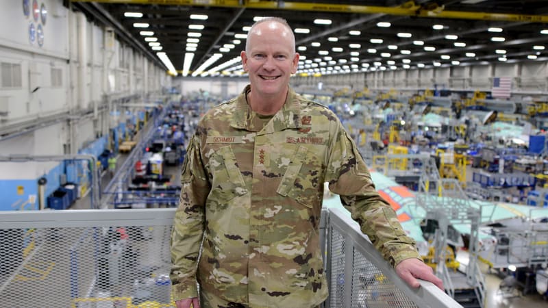 An Air Force general stands on a walkway above a factory floor with green-primed F-35 airframes in assembly jigs