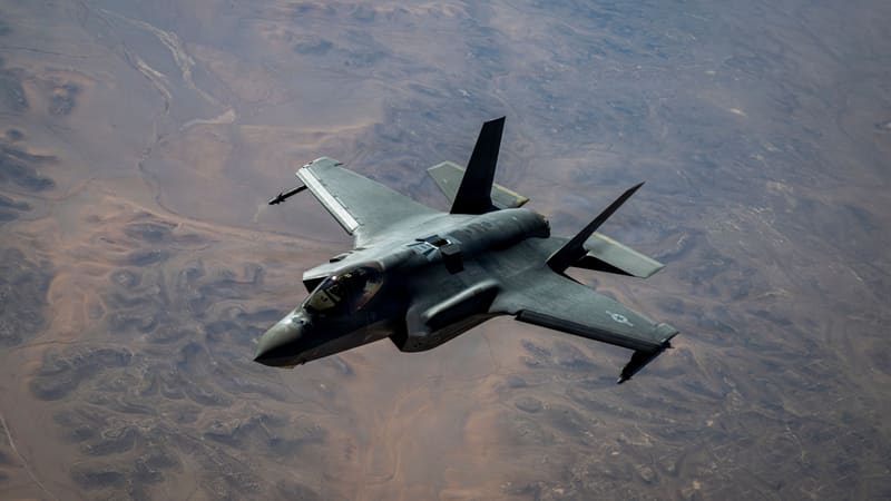 A grey U.S. Air Force F-35A stealth fighter banking in flight high above brown desert terrain