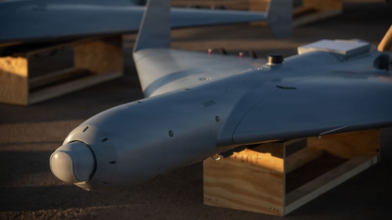 Nose and delta wing of a gray LUCAS drone on a wooden stand, with more LUCAS drones behind