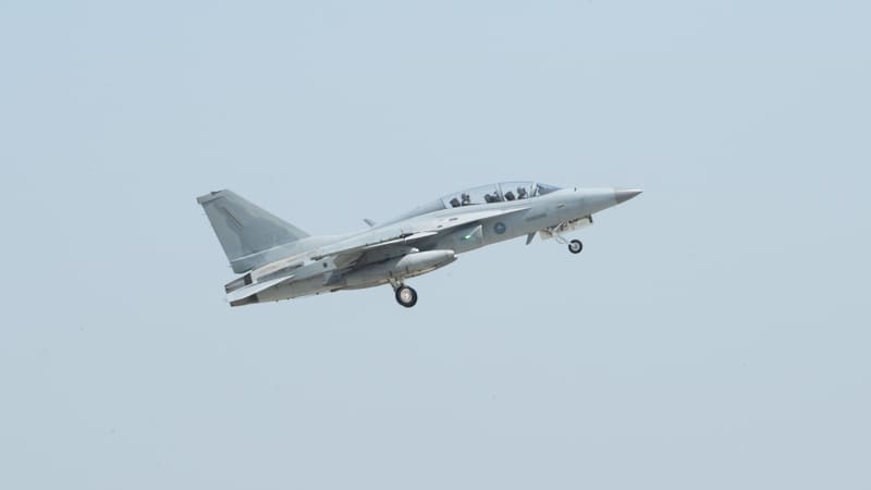 Grey two-seat FA-50 light combat jet climbing away with its landing gear still extended against a pale sky
