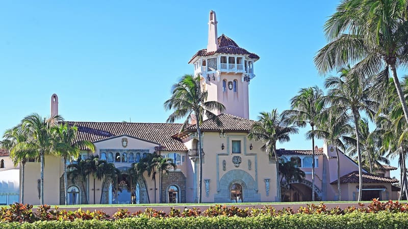 Front of the Mar-a-Lago estate with its tower, palm trees and hedges under a clear sky
