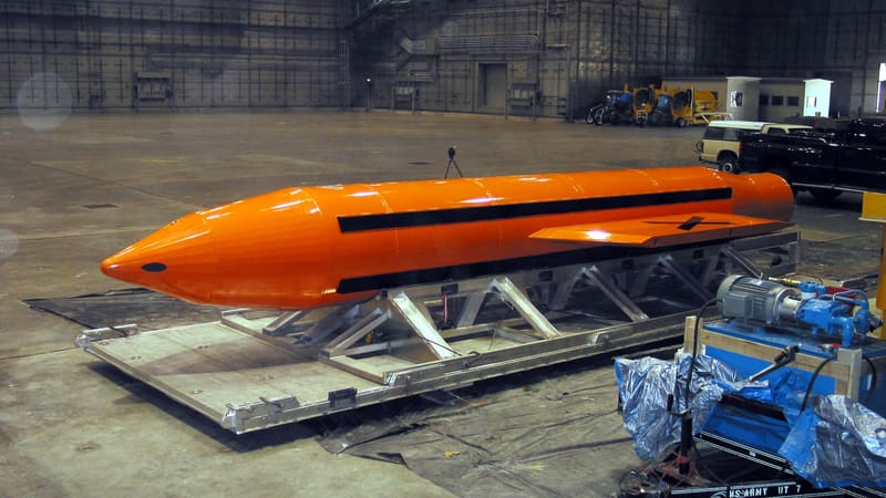 Large orange GBU-43/B MOAB bomb with black stripes on a metal cradle inside a hangar