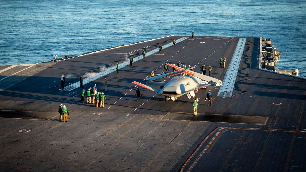 High view of an MQ-25 drone surrounded by deck crew on a carrier flight deck at sea