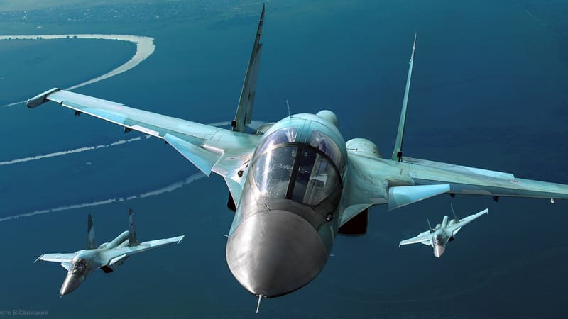 A Russian Su-34 fighter-bomber flies head-on over water with two more Su-34s behind it