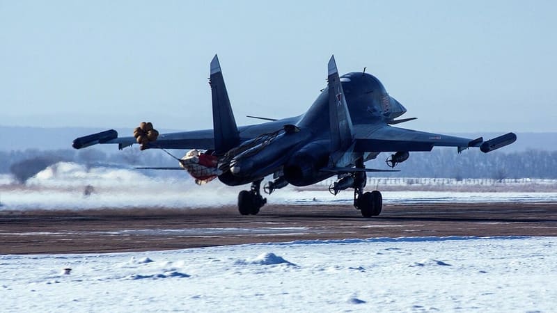 A Su-34 lands on a snowy runway with its braking parachute deploying