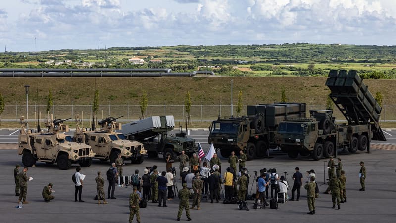 Journalists and soldiers before U.S. MADIS and NMESIS vehicles and Japanese missile launchers on a vehicle lot