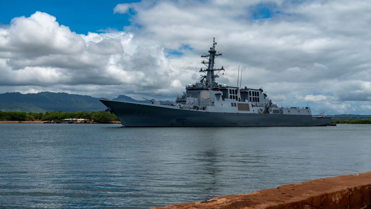Grey South Korean destroyer with hull number 995 entering a harbour under a cloudy sky with mountains behind