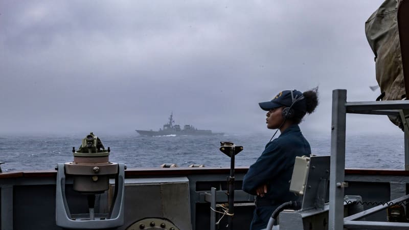A U.S. Navy sailor on a destroyer bridge wing watches a South Korean Aegis destroyer sail through grey seas