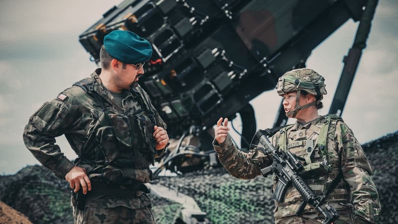 A U.S. soldier gestures as she talks with a Polish officer in a green beret in front of a raised Patriot launcher