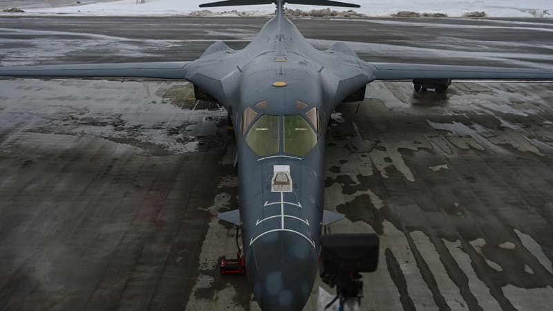 A US Air Force B-1B Lancer bomber parked on a wet apron at an air base, seen from above and in front