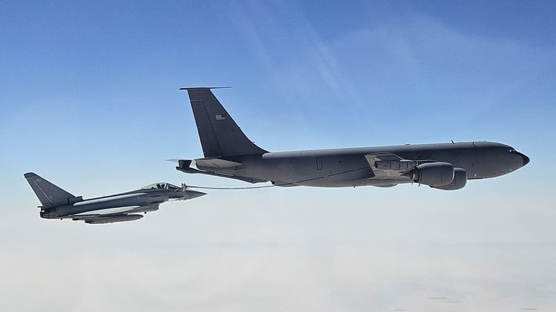 An RAF Typhoon takes fuel by hose from a grey U.S. Air Force KC-135 tanker above a hazy desert