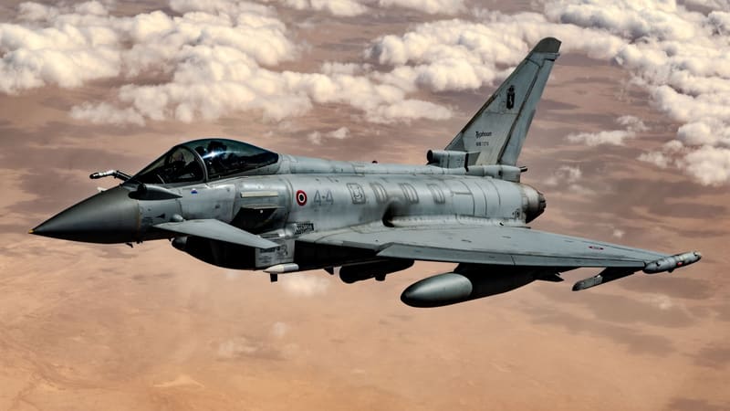 Italian Air Force Eurofighter Typhoon in flight over desert and clouds, carrying an external fuel tank and underwing stores