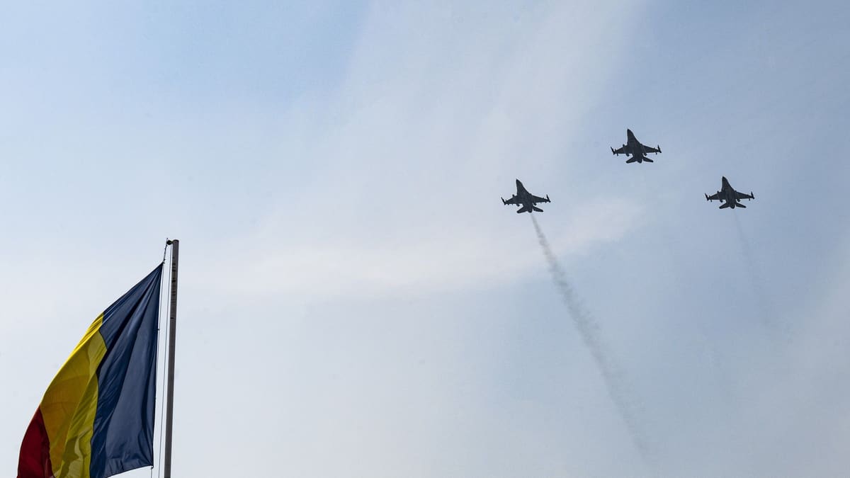 Three F-16 fighters flying in formation over Constanța beside a Romanian flag on a flagpole