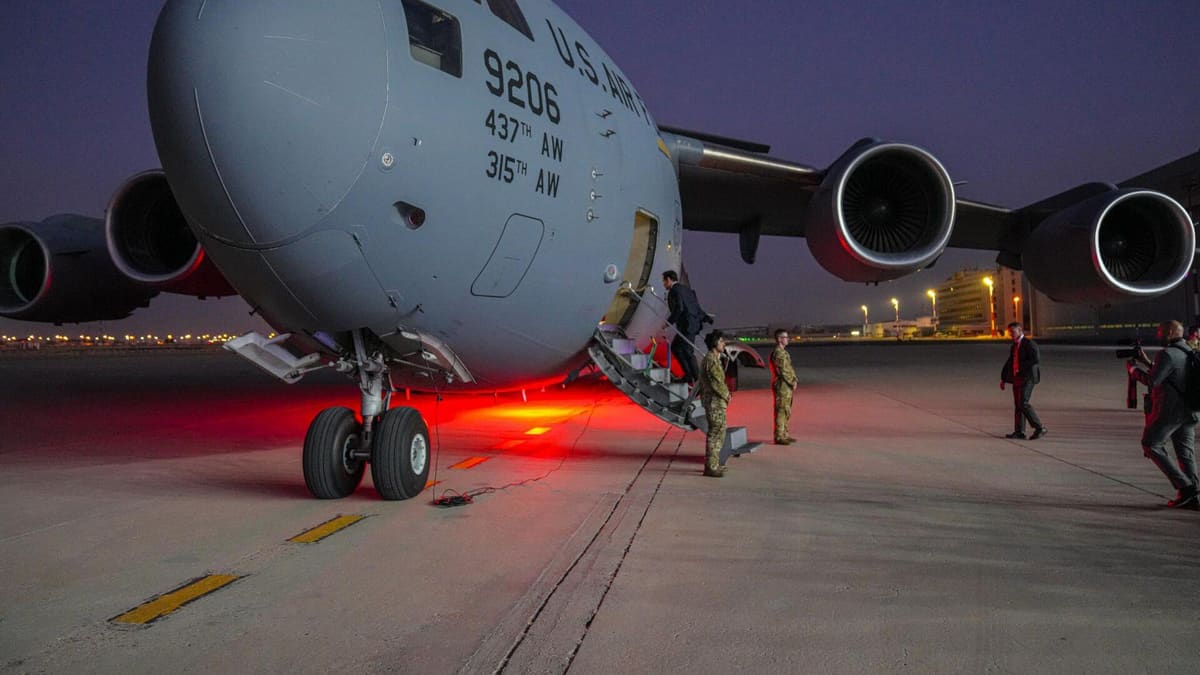 Secretary of State Marco Rubio climbs the steps of a US Air Force C-17 on a floodlit airfield at dusk in Kuwait