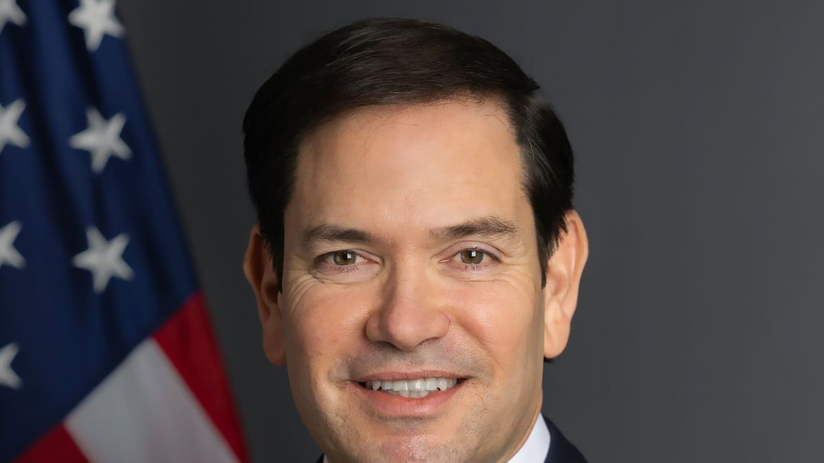 Official portrait of Marco Rubio in a dark suit in front of a US flag