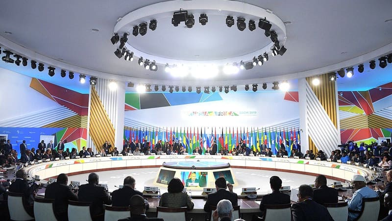 Leaders and delegates seated around a circular table in a hall with a Russia-Africa Sochi 2019 backdrop and flags
