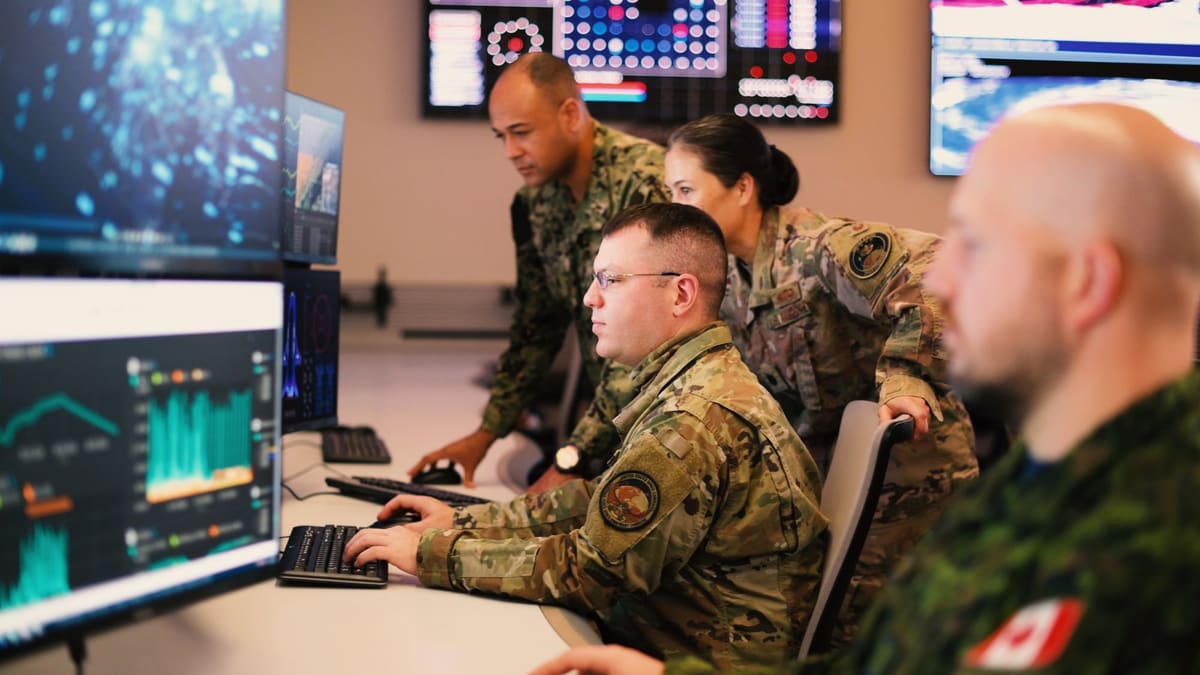 U.S. and Canadian military personnel work at computer screens in a space operations centre