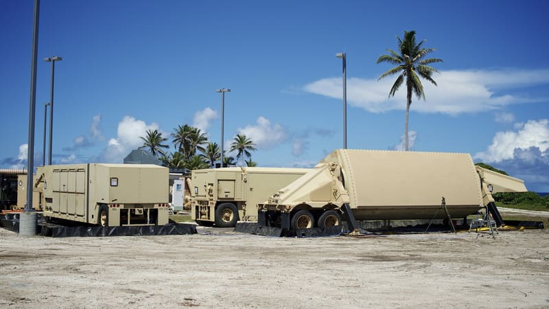 A tan AN/TPY-2 radar and its support trailers set up on open ground among palm trees at Kwajalein Atoll