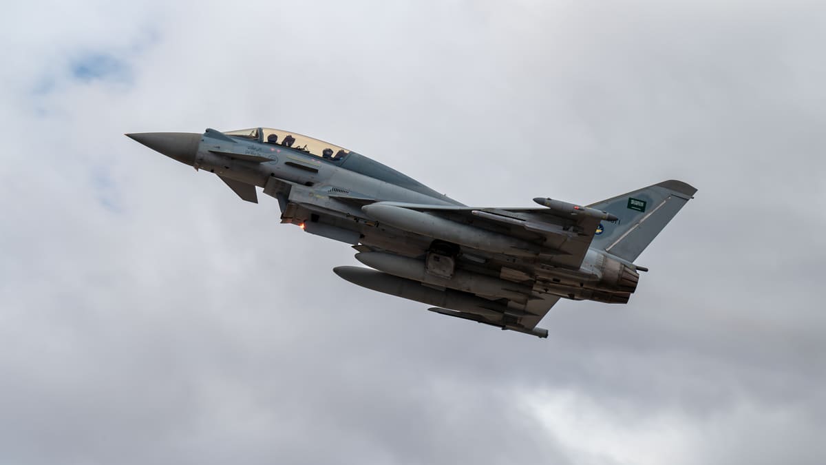 Royal Saudi Air Force Eurofighter Typhoon with Saudi flag on its tail climbing against a cloudy grey sky
