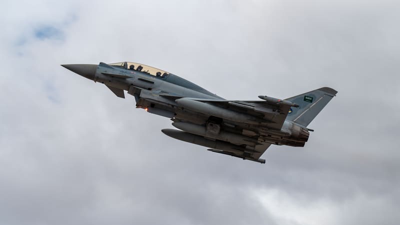 Royal Saudi Air Force Eurofighter Typhoon with Saudi flag on its tail climbing against a cloudy grey sky