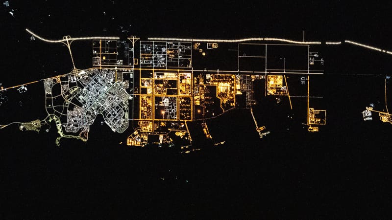 Night view from space of Yanbu's lit city grid and orange-lit industrial zone along the dark Red Sea coast