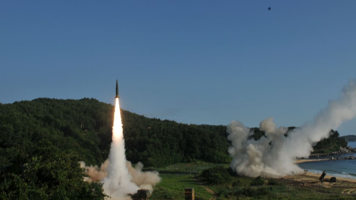 A South Korean Hyunmoo-2 missile lifts off from a wheeled launcher on a wooded coast as a U.S. rocket fires at right