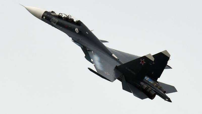 A grey Russian Navy Su-30SM fighter with side number 48 banking in flight against a pale sky