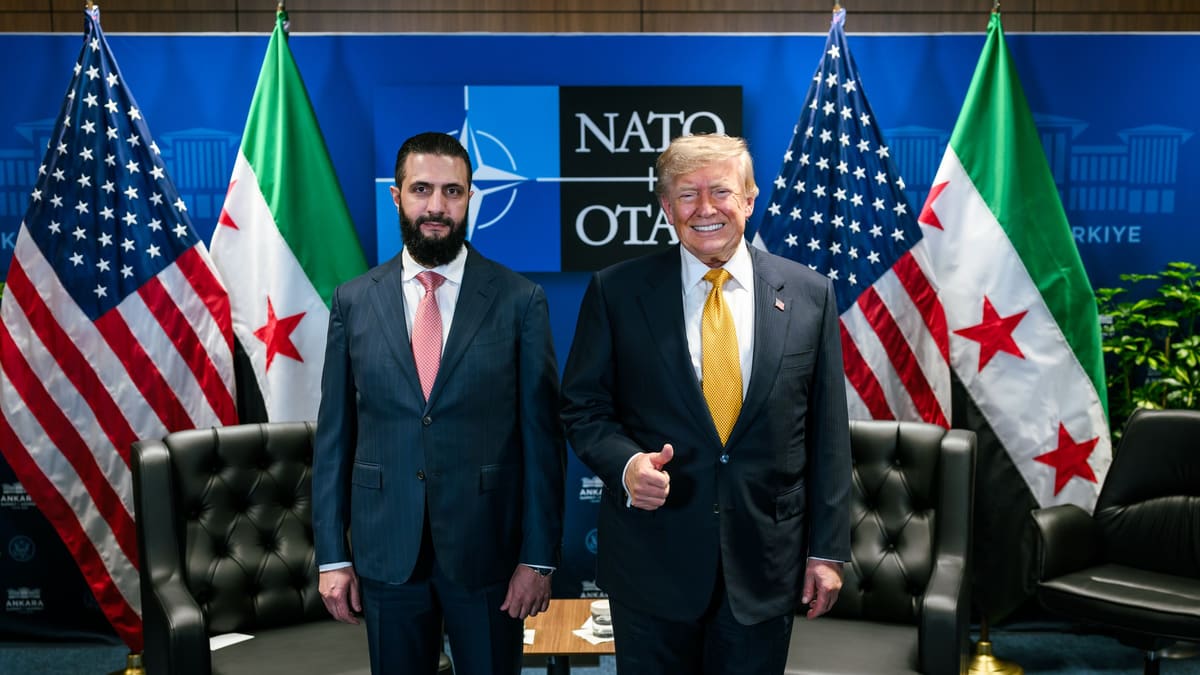 Ahmed al-Sharaa and a smiling Donald Trump stand side by side before US and Syrian flags and a NATO backdrop.