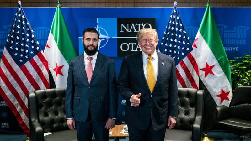 Ahmed al-Sharaa and a smiling Donald Trump stand side by side before US and Syrian flags and a NATO backdrop.