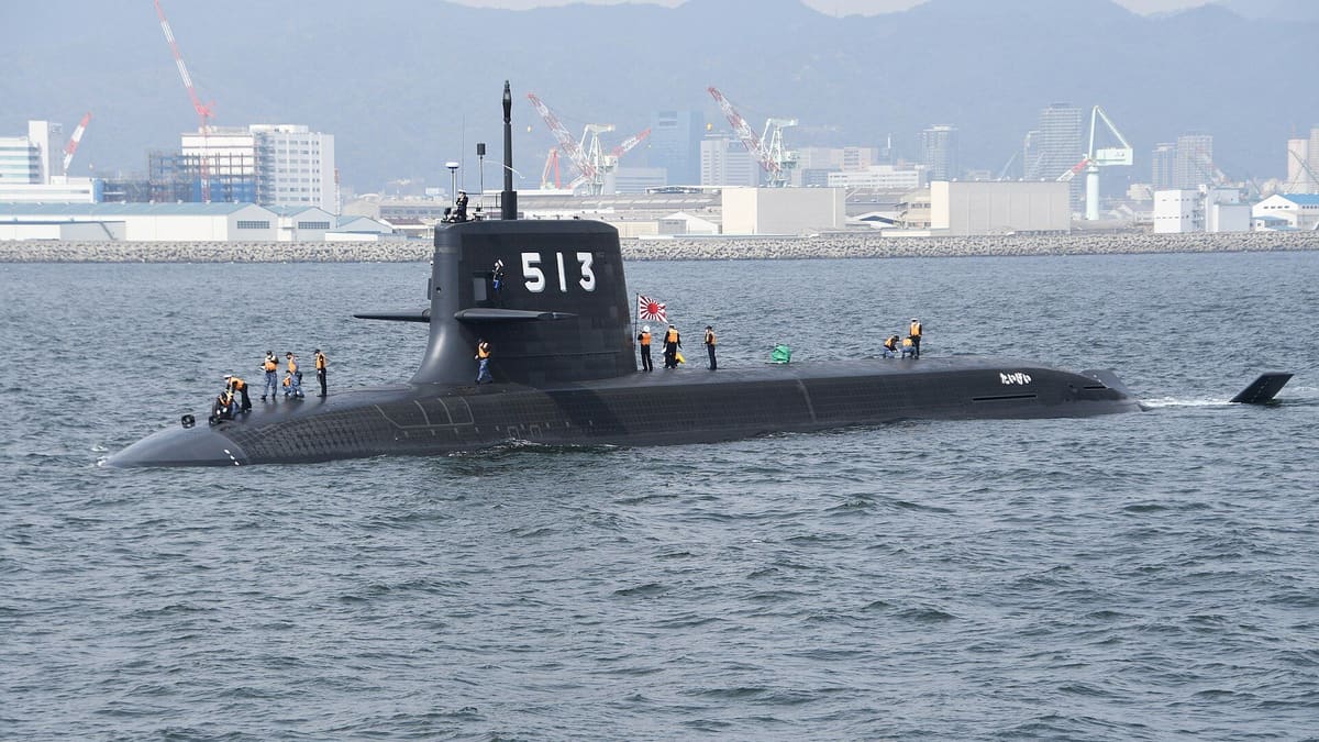 JS Taigei, pennant 513, a black Japanese submarine with crew on deck, leaving Kobe harbor with shipyard cranes behind