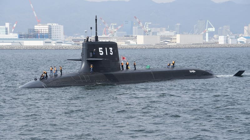 JS Taigei, pennant 513, a black Japanese submarine with crew on deck, leaving Kobe harbor with shipyard cranes behind