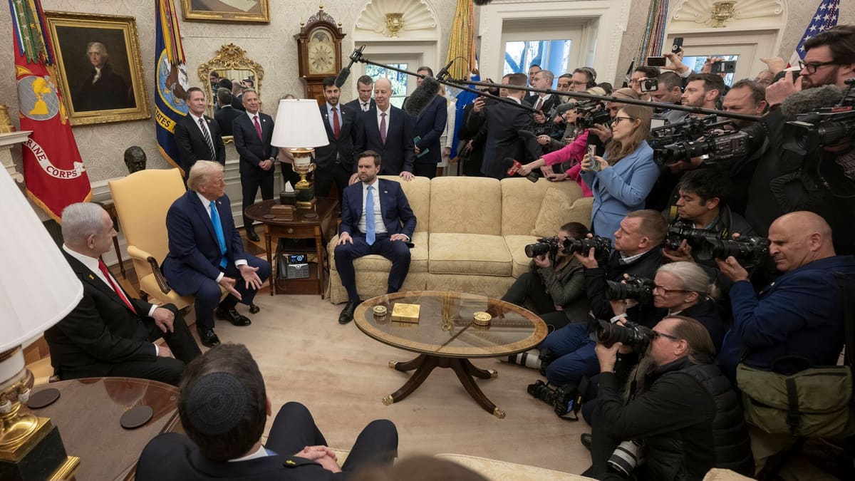Two men talk in armchairs in the Oval Office in 2025 while a crowd of photographers surrounds them