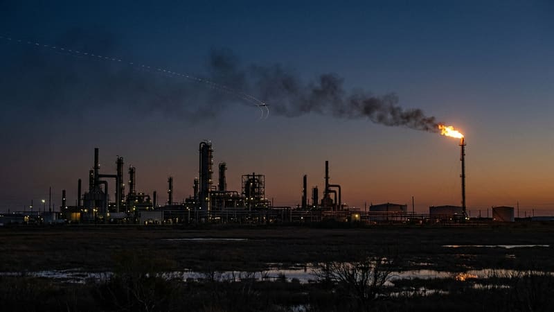 Oil refinery silhouetted at dusk with a burning gas flare and a small aircraft-like shape trailing dotted lights