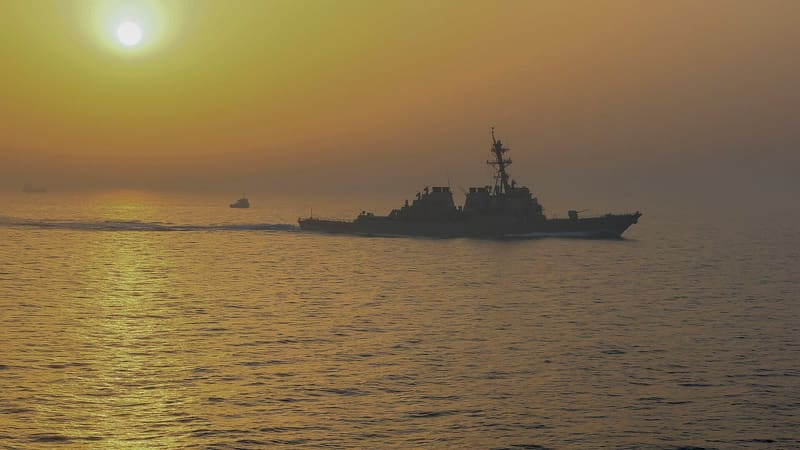 Silhouette of a US Navy destroyer at sea in haze with a small vessel and a distant ship on the horizon